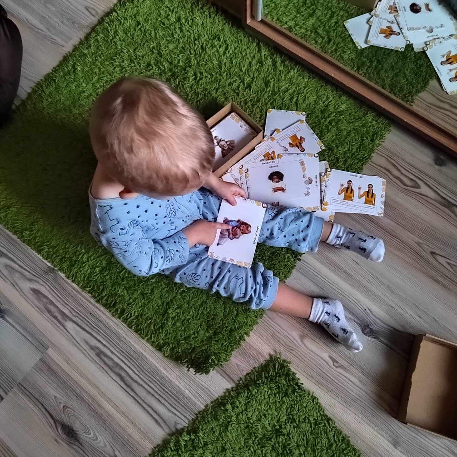 Baba nézegeti a Csemete Jelek babajelbeszéd kártyacsomagot ülve.
